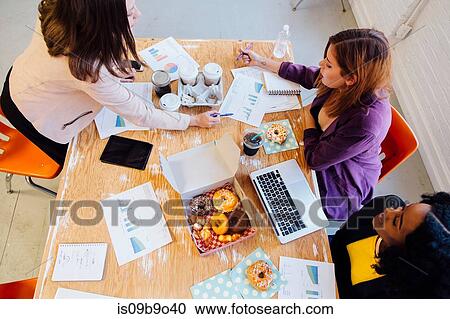 Colleagues working together at desk sharing doughnuts View Large Photo Image Stock Image - Colleagues working together at desk sharing doughnuts. Fotosearch