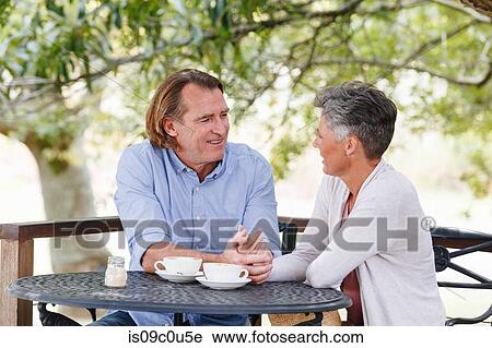 Stock Image - Couple enjoying coffee under shade in garden. Fotosearch