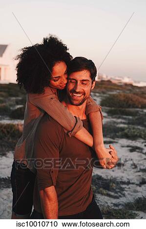 Stock Image - Couple enjoying view of sunset on beach. Fotosearch