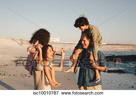 Stock Photo - Couple giving children piggyback ride on beach. Fotosearch