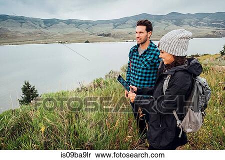 Stock Photography - Couple hiking, standing beside Dillon Reservoir, young woman holding digital tablet, Silverthorne, Colorado, USA. Fotosearch