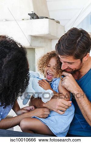Stock Photograph - Couple hugging and tickling daughter in beach house. Fotosearch
