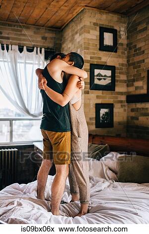 Stock Photo - Couple hugging standing on bed. Fotosearch