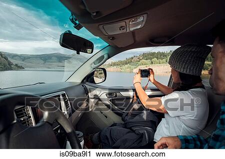 Stock Image - Couple in car, young woman taking photograph through car window, Silverthorne, Colorado, USA. Fotosearch