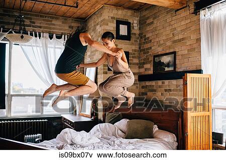 Stock Photo - Couple jumping on bed. Fotosearch