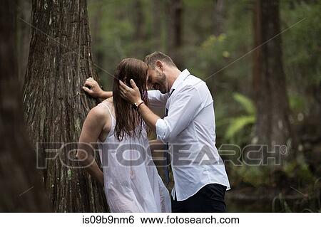 Couple leaning against tree kissing View Large Photo Image Stock Photograph - Couple leaning against tree kissing. Fotosearch