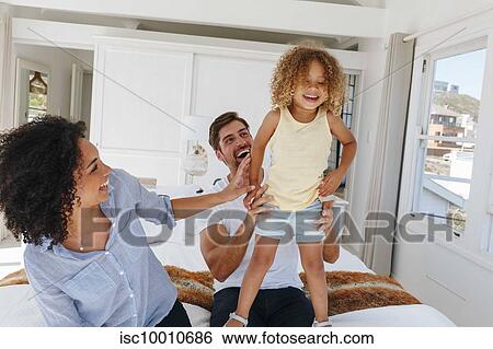 Couple playing with daughter on bed in beach house View Large Photo Image Stock Photograph - Couple playing with daughter on bed in beach house. Fotosearch