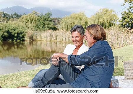 Stock Image - Couple relaxing by pond, Cape Town, South Africa. Fotosearch