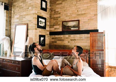 Couple sitting cross legged laughing on bed View Large Photo Image Stock Image - Couple sitting cross legged laughing on bed. Fotosearch