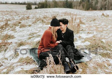 Stock Photograph - Couple sitting on blanket on frozen ground, Georgetown, Canada. Fotosearch