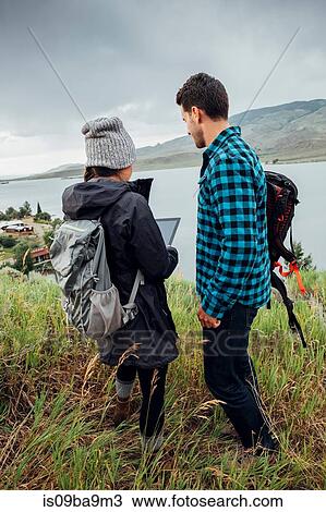 Stock Image - Couple standing beside Dillon Reservoir, using digital tablet, Silverthorne, Colorado, USA. Fotosearch