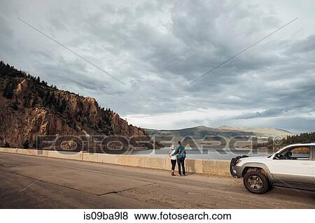 Stock Photo - Couple standing on road beside Dillon Reservoir, looking at view, Silverthorne, Colorado, USA. Fotosearch