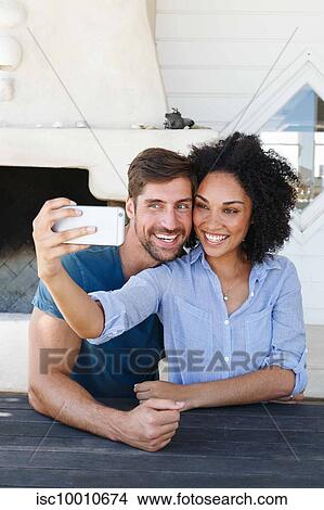Picture - Couple taking selfie in beach house. Fotosearch