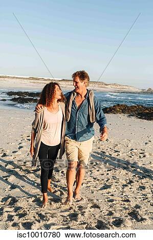 Stock Image - Couple taking walk on sandy beach. Fotosearch