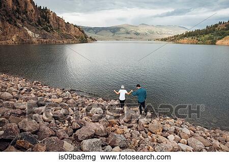 Stock Image - Couple walking on rocks beside Dillon Reservoir, elevated view, Silverthorne, Colorado, USA. Fotosearch