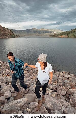 Stock Image - Couple walking on rocks beside Dillon Reservoir, elevated view, Silverthorne, Colorado, USA. Fotosearch