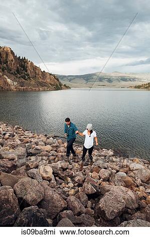 Stock Image - Couple walking on rocks beside Dillon Reservoir, elevated view, Silverthorne, Colorado, USA. Fotosearch