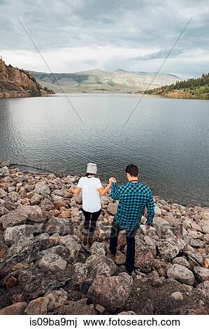 Stock Image - Couple walking on rocks beside Dillon Reservoir, elevated view, Silverthorne, Colorado, USA. Fotosearch