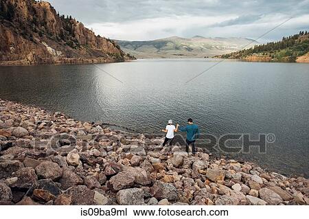 Stock Image - Couple walking on rocks beside Dillon Reservoir, elevated view, Silverthorne, Colorado, USA. Fotosearch