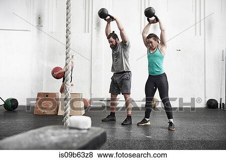 Stock Photo - Couple working out with kettlebells in cross training gym. Fotosearch