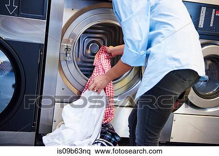 Stock Photography - Cropped shot of woman inserting laundry into washing machine at laundrette. Fotosearch