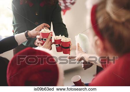 Stock Image - Cropped shot of young woman handing out popcorn at christmas party. Fotosearch