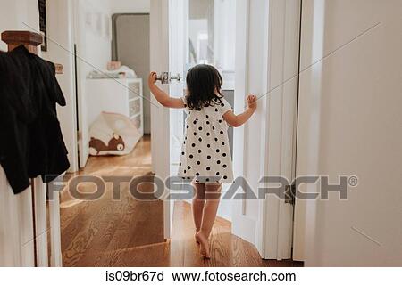 Stock Image - Curious girl opening door. Fotosearch