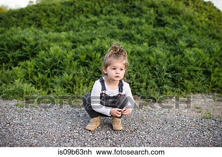 Stock Image - Cute girl crouching on dirt track looking away. Fotosearch