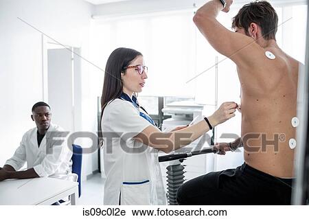 Stock Image - Doctor watching nurse perform ECG test on patient in consultation room. Fotosearch