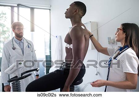 Stock Photograph - Doctor watching nurse perform ECG test on patient in consultation room. Fotosearch