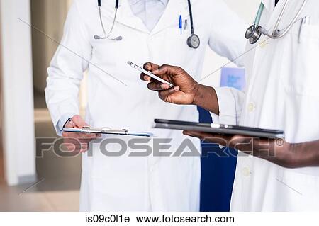 Stock Image - Doctors using smartphone at hospital reception. Fotosearch