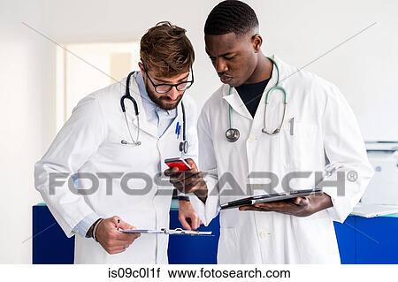 Stock Image - Doctors using smartphone at hospital reception. Fotosearch