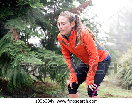 Stock Photo - Exhausted female runner bending forward with hands on knees in park. Fotosearch