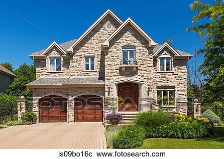 Stock Image - Facade of luxury house in cut stone with shrubs and flowers in garden border. Fotosearch