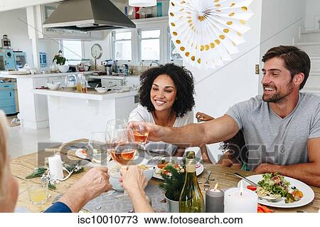 Stock Image - Family toasting wine at dining table in home party. Fotosearch