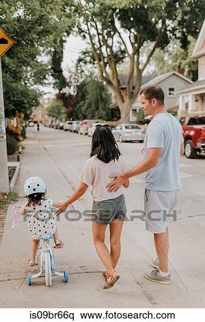 Stock Photography - Family walking with daughter on tricycle. Fotosearch