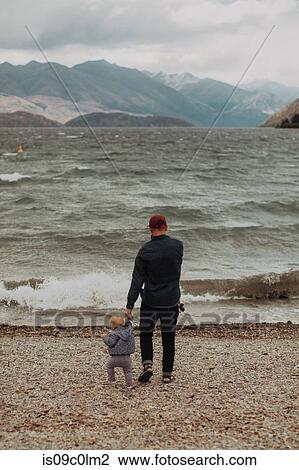 Stock Image - Father and baby on beach, Queenstown, Canterbury, New Zealand. Fotosearch