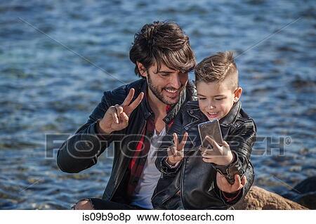 Father and son beside sea, son taking selfie using smartphone View Large Photo Image Stock Photography - Father and son beside sea, son taking selfie using smartphone. Fotosearch