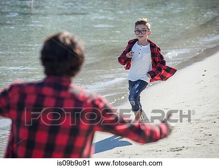 Stock Image - Father and son on beach, son running towards father. Fotosearch