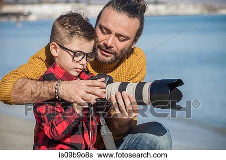 Stock Photograph - Father and son outdoors, father teaching son to use camera. Fotosearch