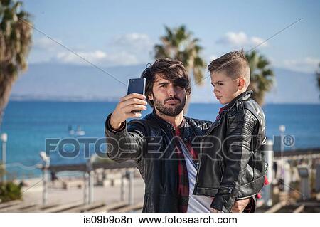 Father and son outdoors, father taking selfie using smartphone View Large Photo Image Picture - Father and son outdoors, father taking selfie using smartphone. Fotosearch