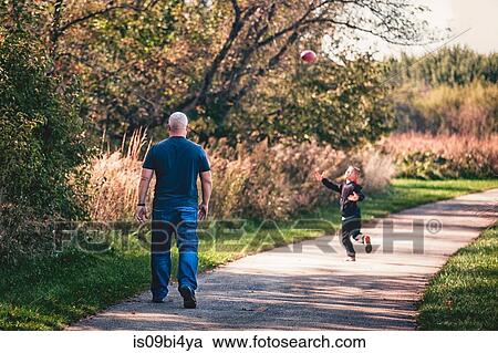 Stock Image - Father and son playing with ball on pathway. Fotosearch
