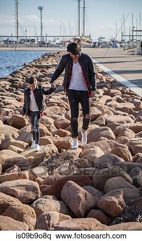 Stock Photography - Father and son walking on rocks beside sea. Fotosearch