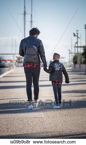 Stock Photography - Father and son walking outdoors, holding hands, rear view. Fotosearch