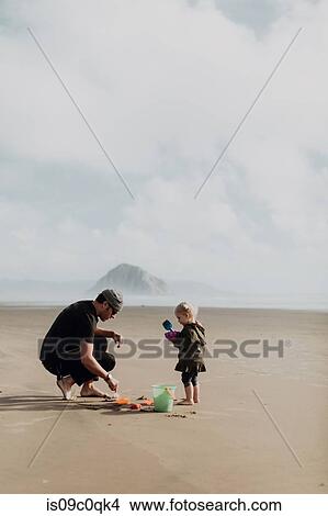 Picture - Father and toddler playing with sand on beach, Morro Bay, California, United States. Fotosearch