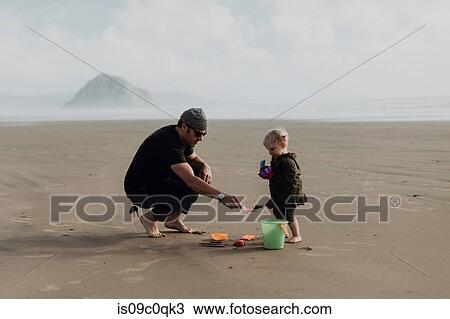 Stock Image - Father and toddler playing with sand on beach, Morro Bay, California, United States. Fotosearch