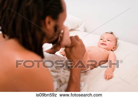 Stock Photo - Father kissing baby son's bare feet on bed. Fotosearch