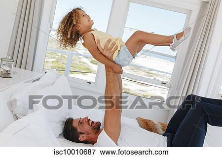 Father lifting daughter in mid air on bed in beach house View Large Photo Image Stock Photo - Father lifting daughter in mid air on bed in beach house. Fotosearch