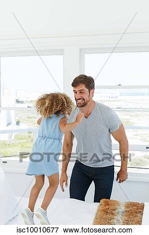 Father playing with daughter jumping on bed in beach house View Large Photo Image Stock Photo - Father playing with daughter jumping on bed in beach house. Fotosearch