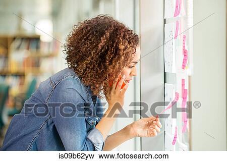 Female digital designer making phone call and looking at adhesive notes on office wall View Large Photo Image Stock Photo - Female digital designer making phone call and looking at adhesive notes on office wall. Fotosearch